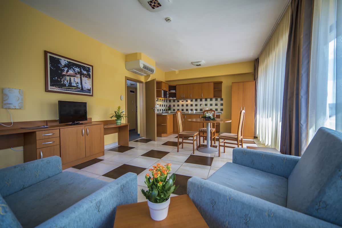 A living room with a sofa, a coffee table with flowers, a TV, and a kitchen area with cabinets and a dining table.