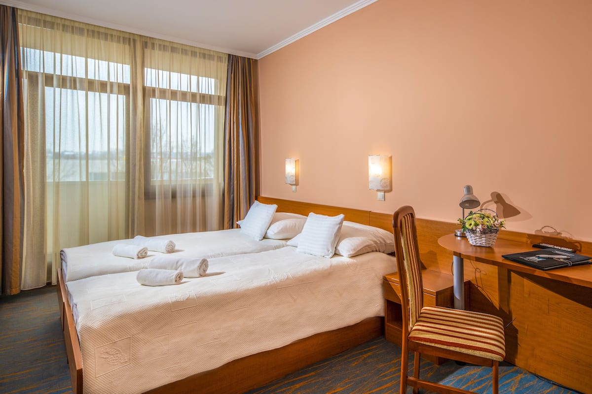 A hotel room with two beds, a desk, a chair, and a window with curtains.