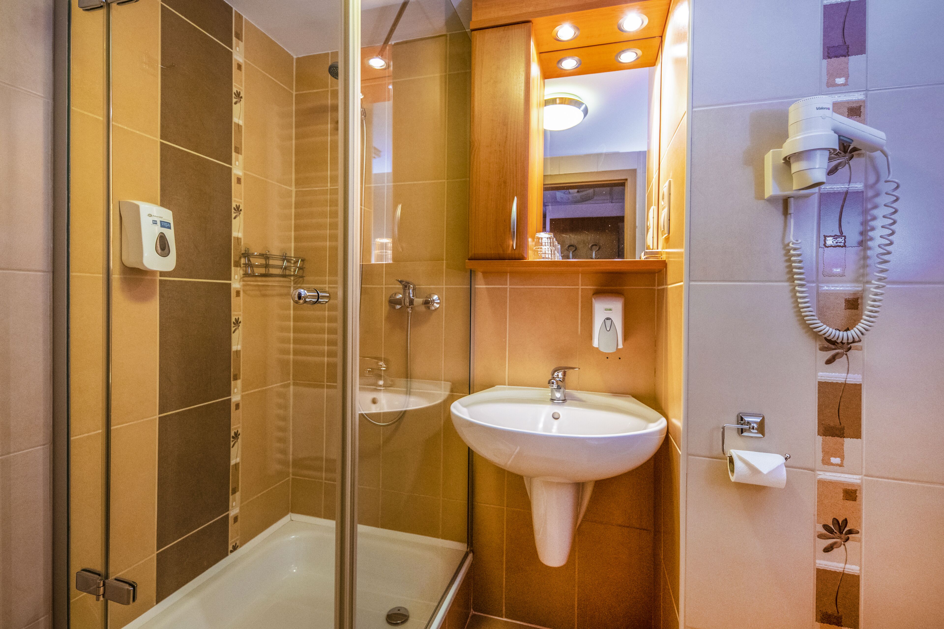 A bathroom with a glass-enclosed shower, a sink, and a hairdryer mounted on the wall.