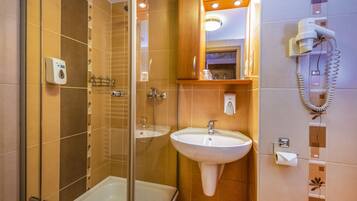 A bathroom with a glass-enclosed shower, a sink, and a hairdryer mounted on the wall.