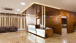 A modern reception area with a wooden reception desk, a sofa, and a staircase. - Crystal Inn (Chikkamagaluru)
