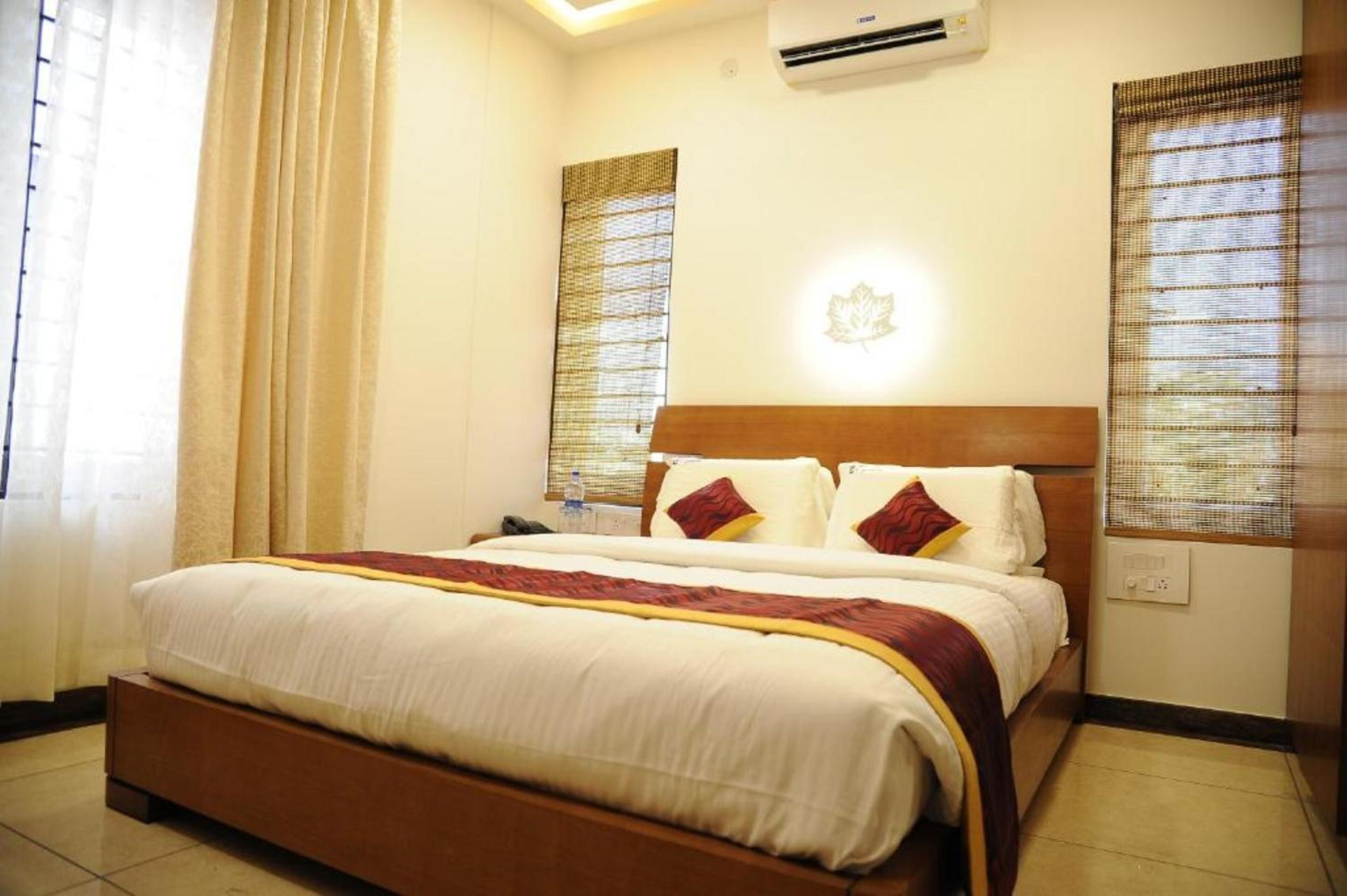 A hotel room with a large bed, a wooden headboard, and a wall-mounted air conditioner.
