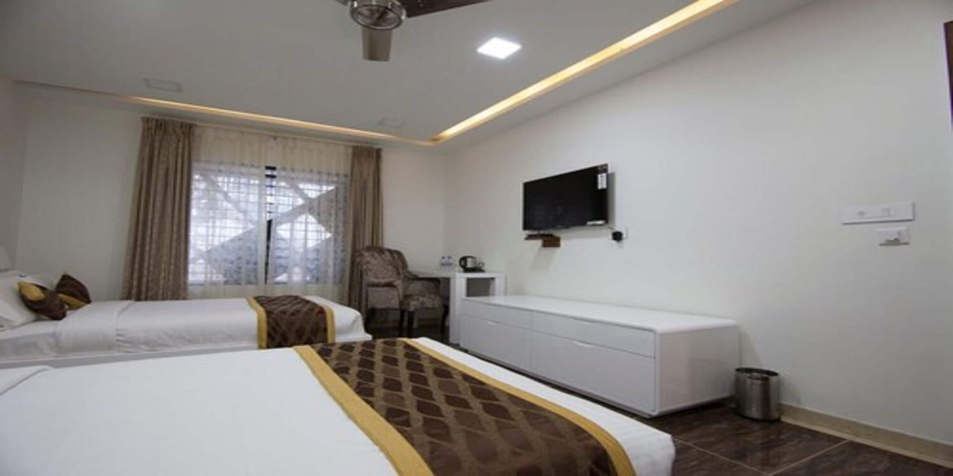 Habitación de hotel con dos camas, un televisor montado en la pared, un escritorio con una silla y un cubo de basura.