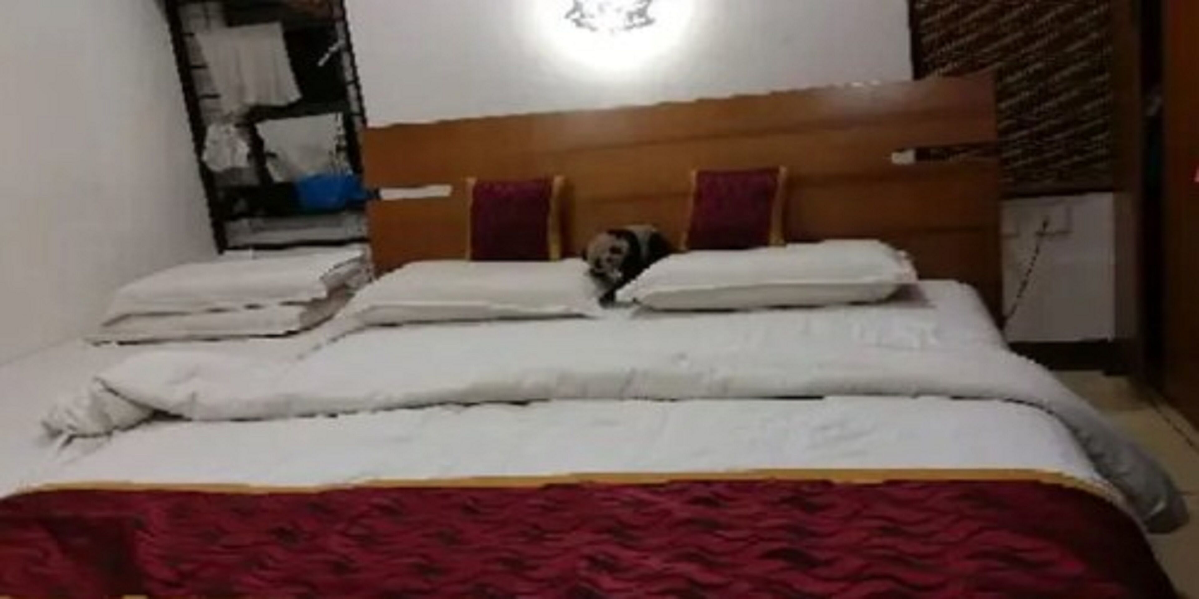 A bed with a wooden headboard, white bedding, and a red blanket.
