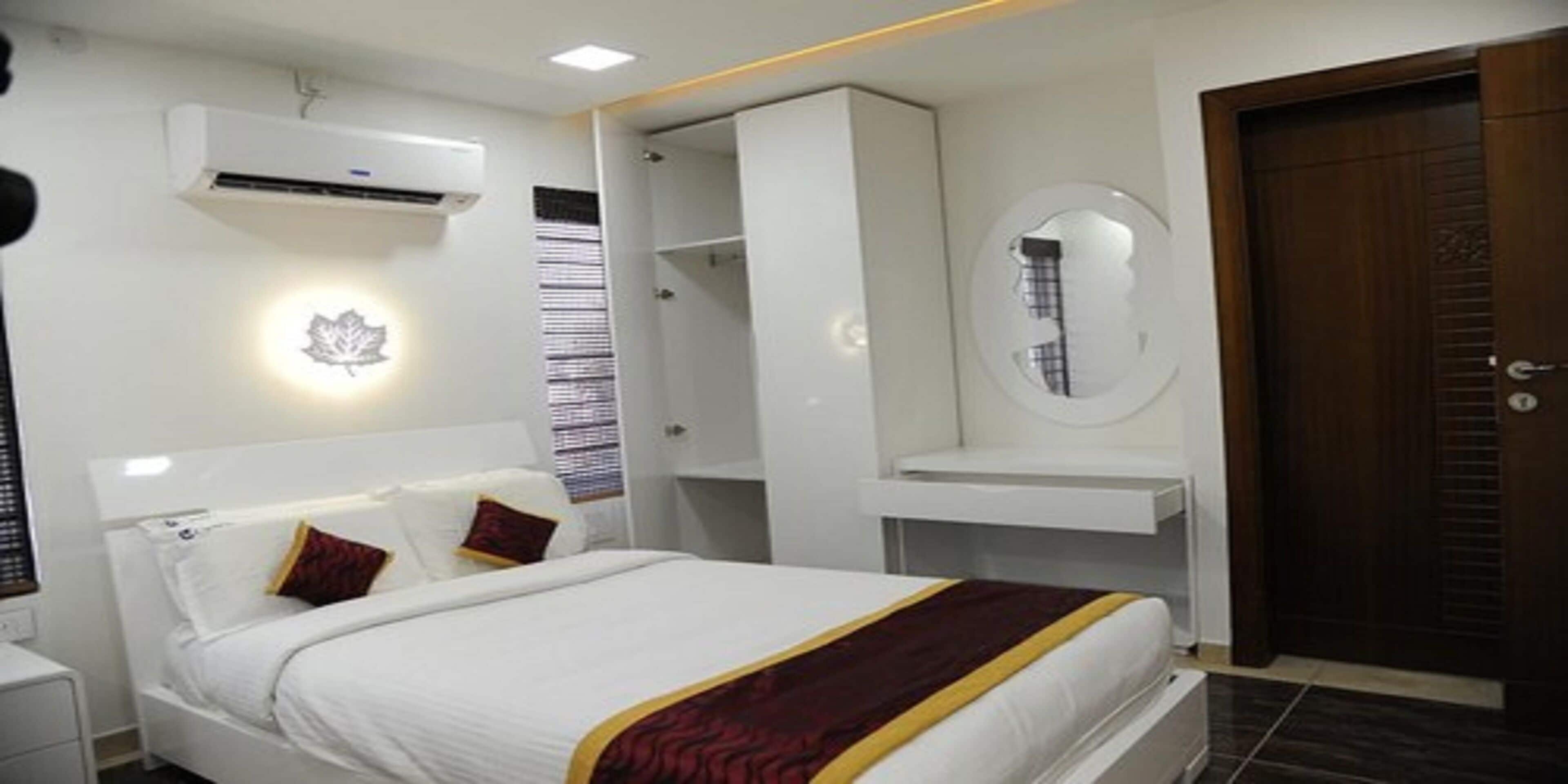 A hotel room with a bed, a bedside table, a mirror, a wardrobe, and an air conditioning unit.