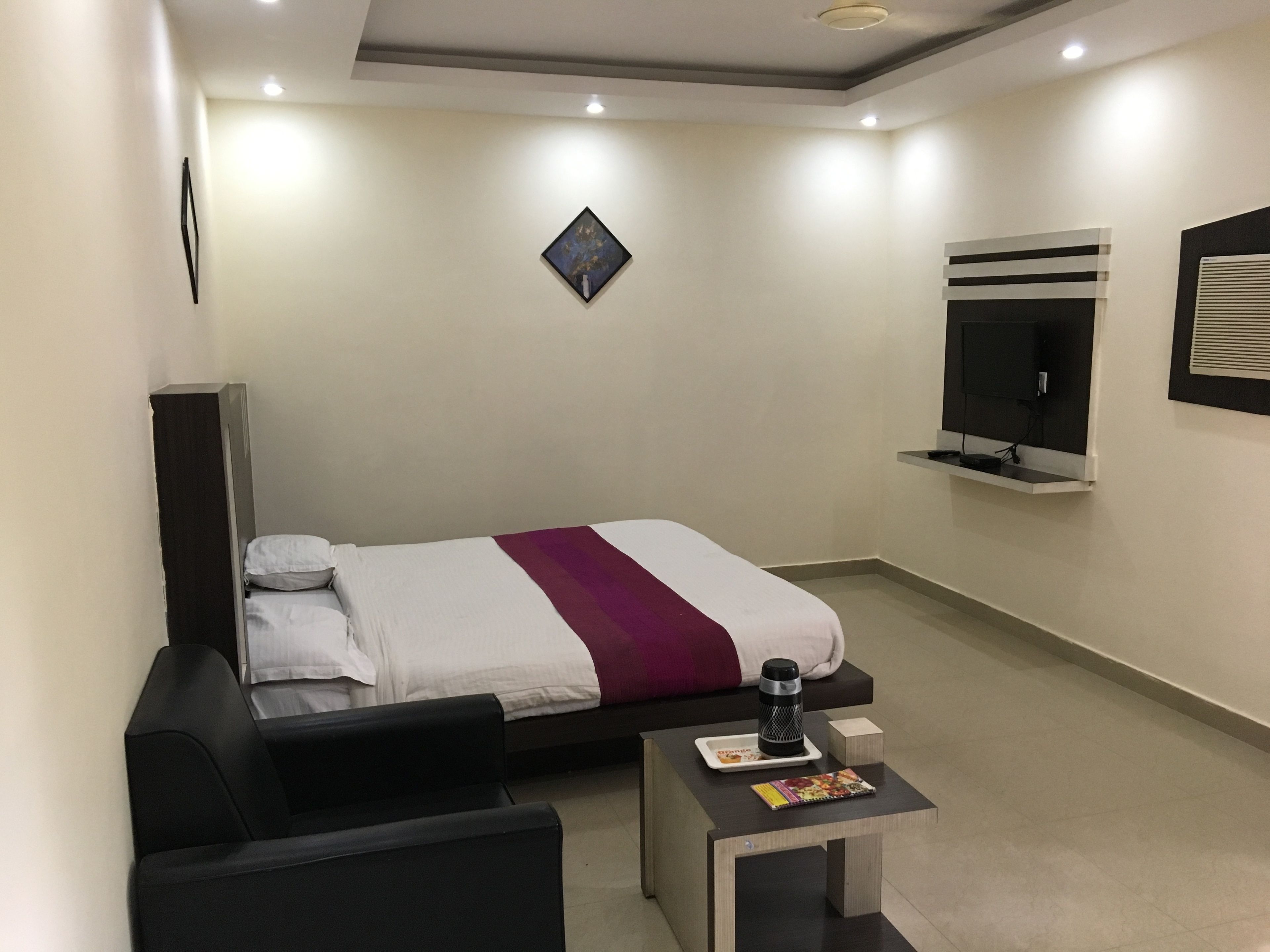 A hotel room with a bed, a small table with a magazine, a coffee maker, and a TV mounted on the wall.
