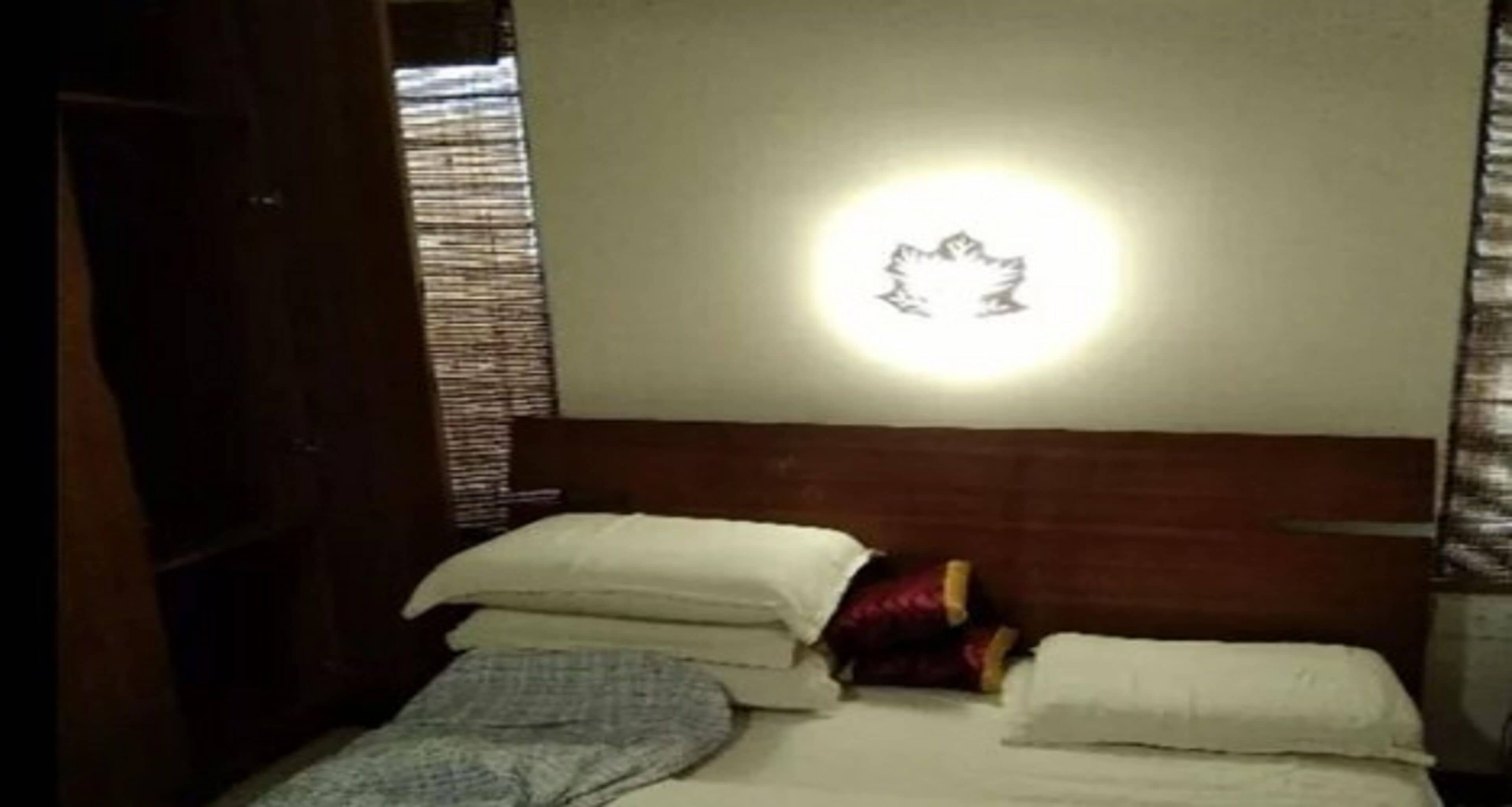 A bedroom with a bed, pillows, and a wall-mounted light fixture.