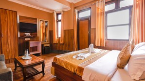 Een hotelkamer met een groot bed, een aan de muur bevestigde televisie, houten meubels en een raam met gordijnen.
