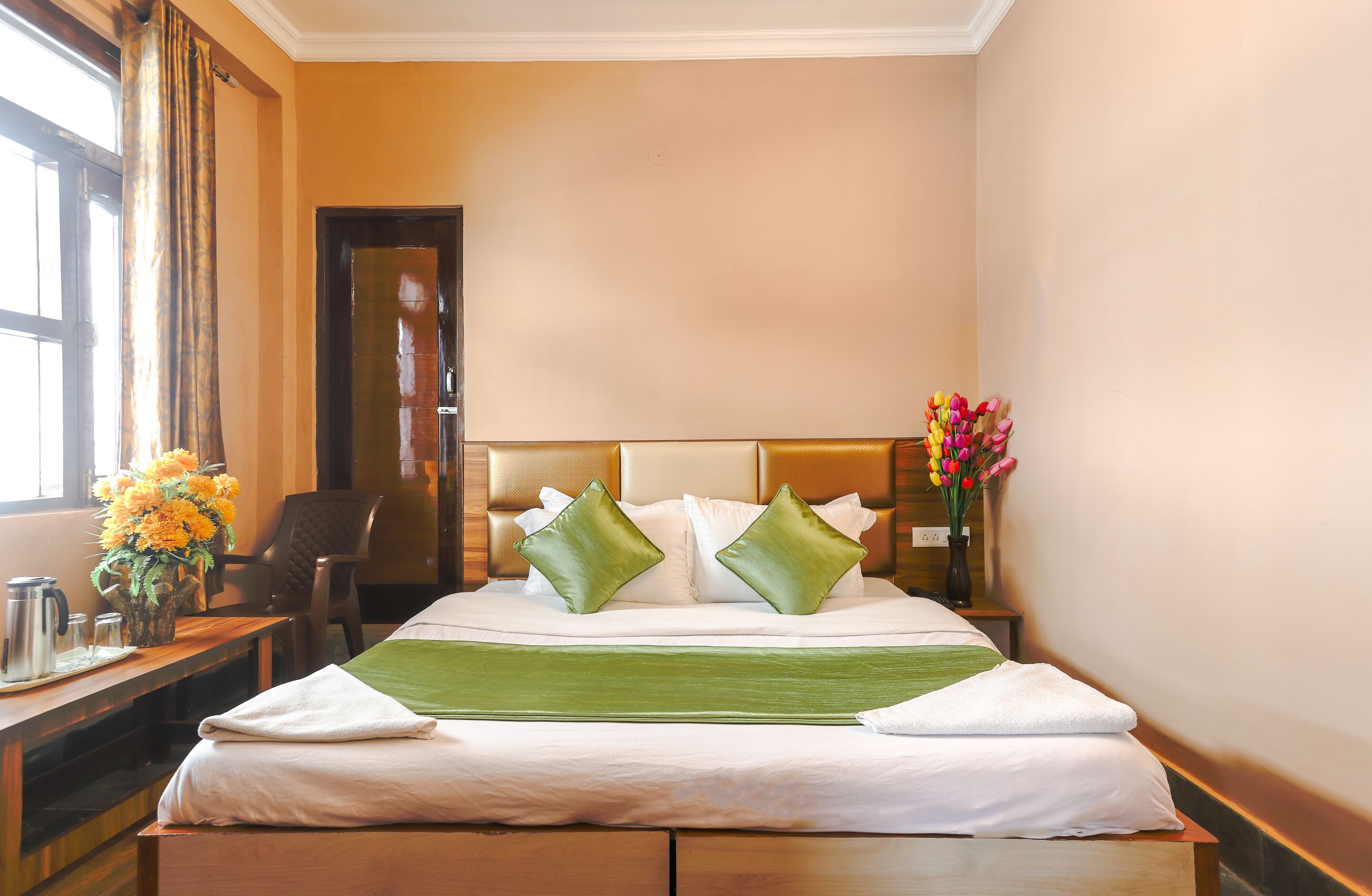 A hotel room with a bed, a desk with a vase of flowers, and a chair.