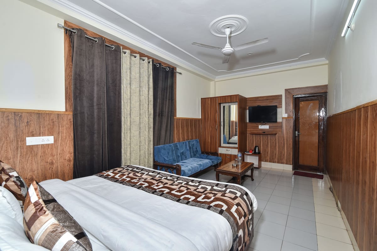 Une chambre d’hôtel avec un lit, un canapé bleu, une armoire en bois, une télévision et un ventilateur de plafond.
