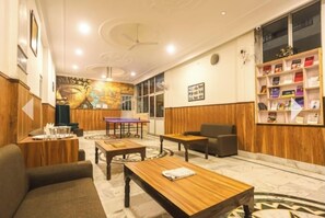 Un hall d’hôtel avec des boiseries, une grande fresque murale, une table de ping-pong et une bibliothèque remplie de livres.