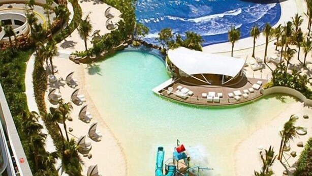 A resort with a large pool, a water slide, and lounge areas with palm trees.