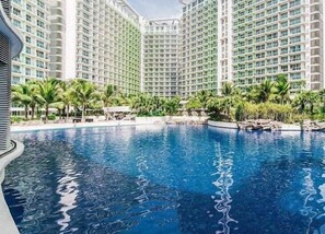 Una gran piscina rodeada de edificios altos con balcones, palmeras y un cielo despejado.