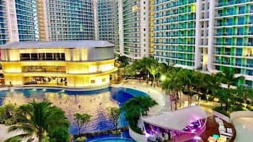 A multi-story hotel with a central pool area, surrounded by lush greenery and palm trees.
