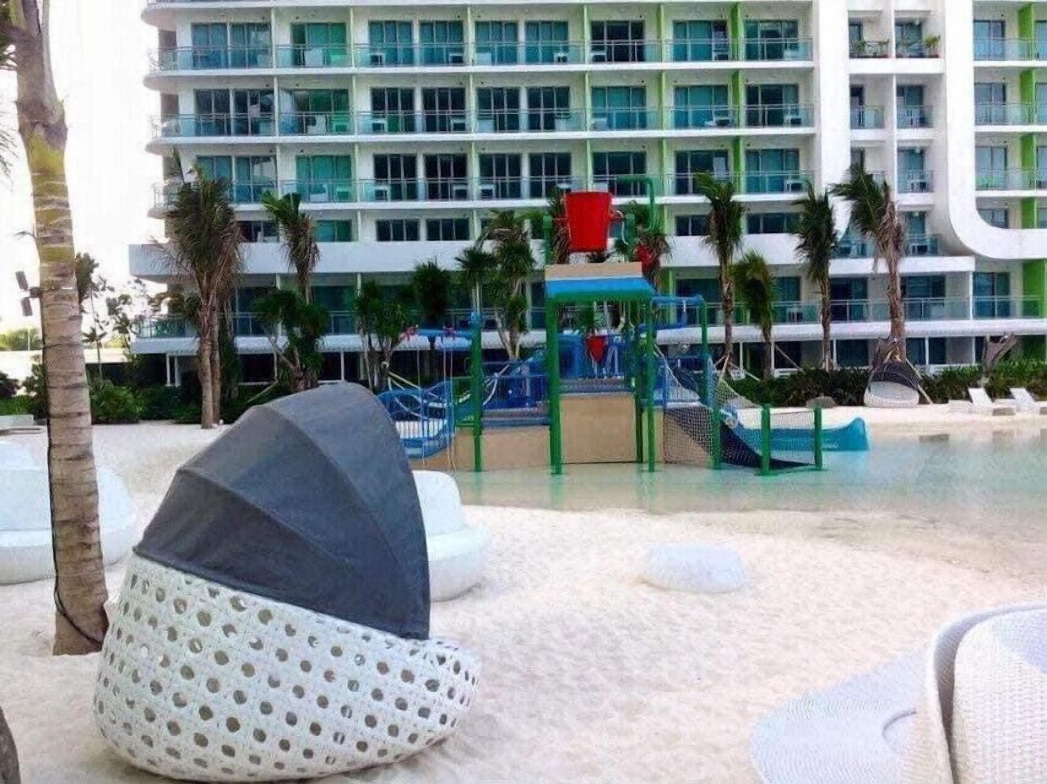 Un hotel moderno con piscina, palmeras y una zona de juegos para niños.