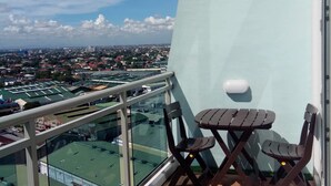 A balcony with a view of a cityscape, a table, and two chairs.