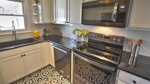 Uma cozinha com armários brancos, micro-ondas de aço inoxidável, forno duplo e painel decorativo.