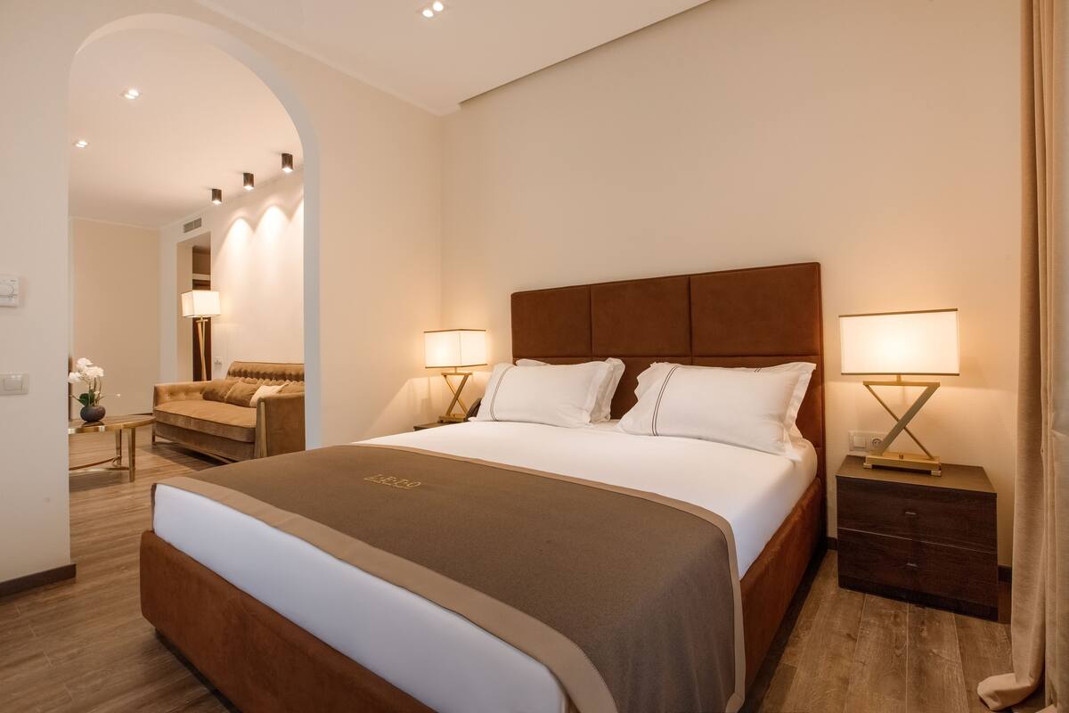 Ein Hotelzimmer mit einem großen Bett, zwei Nachttischen mit Lampen, einem Holzkopfende und einer kleinen Sitzecke mit Sofa und Tisch.