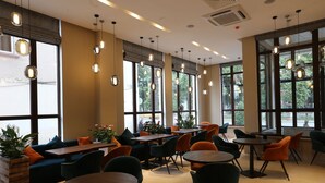 A spacious indoor area with multiple tables and chairs, large windows with views of greenery, and hanging pendant lights. - LETO Boutique Hotel (Zugdidi)