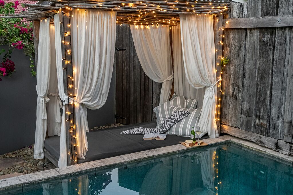 Un rincón exterior acogedor con toldo, luces colgantes y piscina.