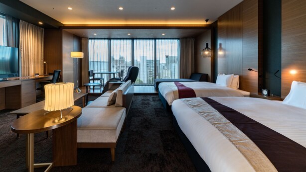 A hotel room with two beds, a desk, a chair, a sofa, and a large window with a city view. - Daiwa Roynet Hotel Hakata Reisen PREMIER (Fukuoka)