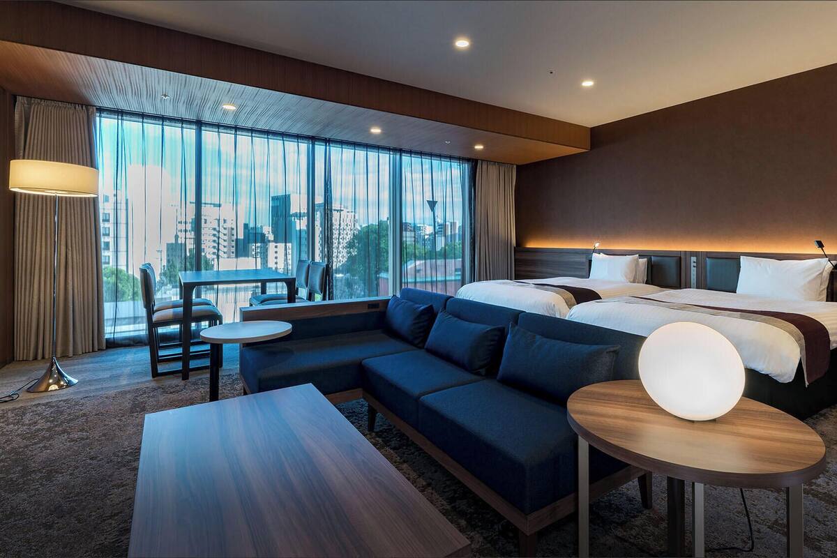 Une chambre d’hôtel moderne, dotée d’un grand lit, d’un canapé, d’une table à manger et offrant une vue sur la ville.