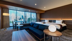 A modern hotel room with a large bed, a sofa, a dining table, and a view of the city through large windows. - Daiwa Roynet Hotel Hakata Reisen PREMIER (Fukuoka)