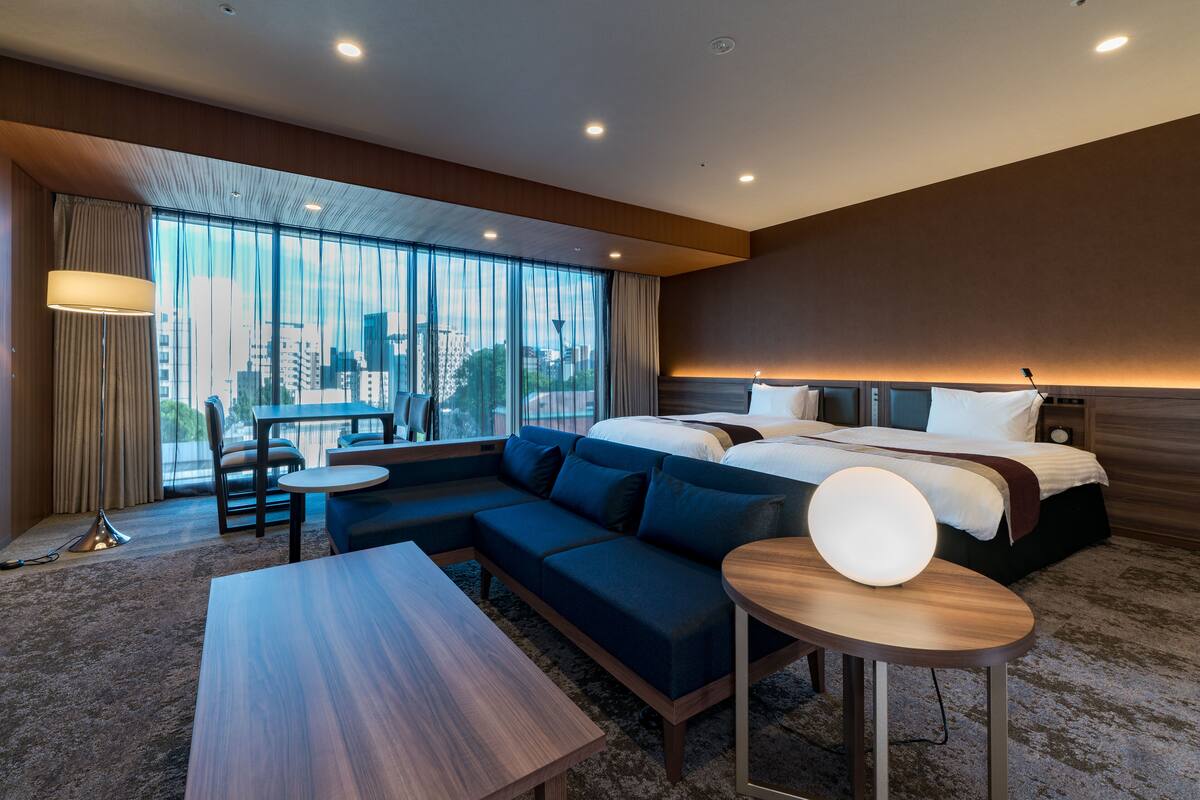 Une chambre d’hôtel moderne dotée d’un grand lit, d’un canapé, d’une table à manger et offrant une vue sur la ville grâce à de grandes fenêtres.