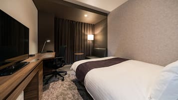 A hotel room with a bed, a desk with a computer, a chair, a TV, and a lamp.