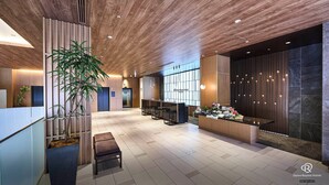 A modern hotel lobby with a reception desk, seating area, and a large potted plant. - Daiwa Roynet Hotel Hakata Reisen PREMIER (Fukuoka)