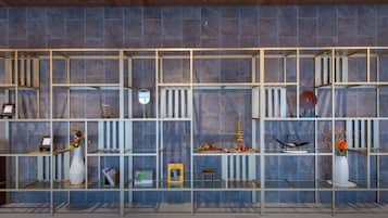 A modern hotel lobby with a blue-tiled wall and a wooden ceiling. There are glass shelves with various decorative items and a small table.