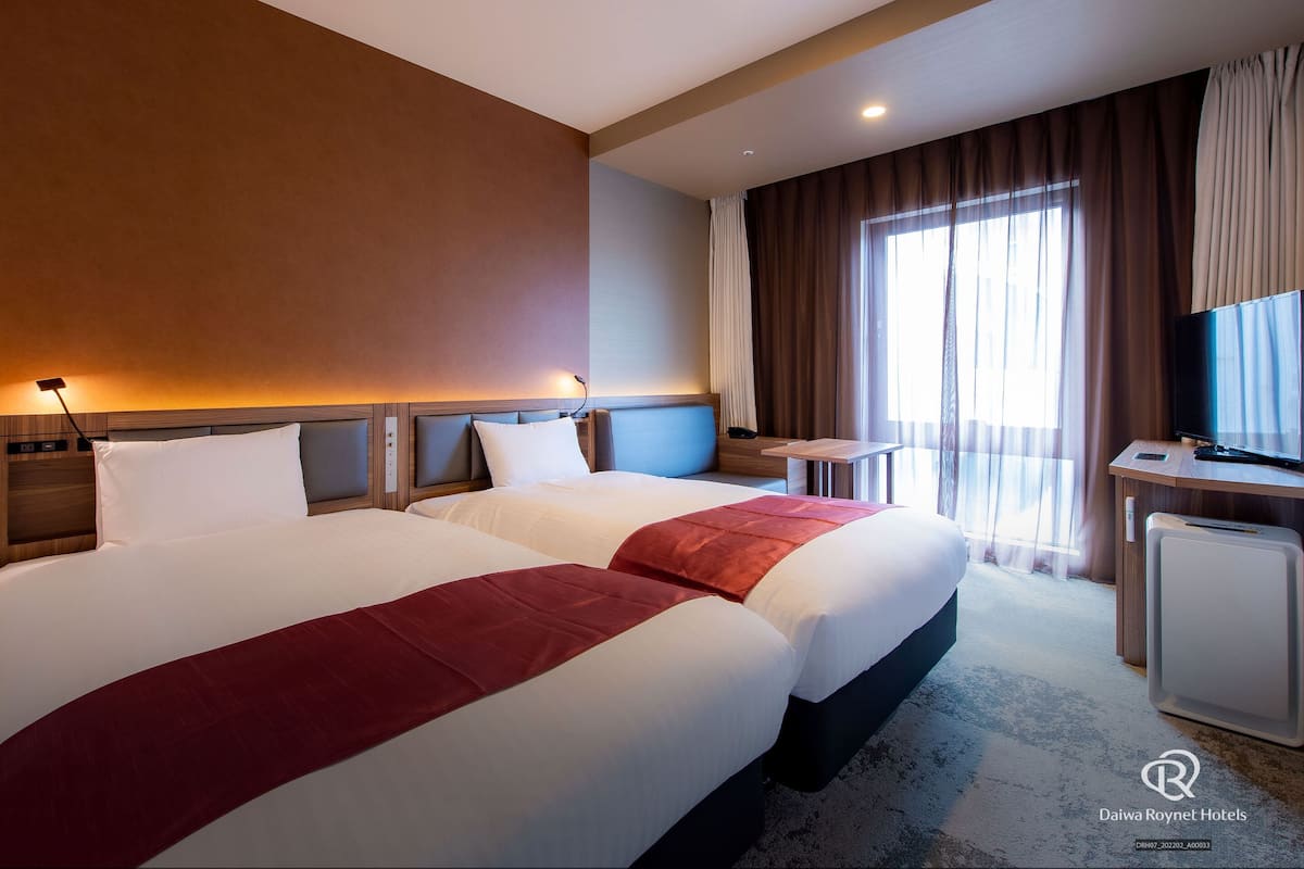 Une chambre d’hôtel avec deux lits, un bureau, une télévision et une fenêtre avec des rideaux.