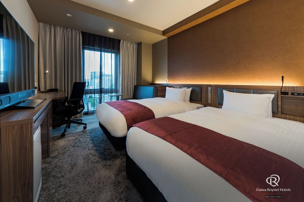 Une chambre d’hôtel avec deux lits, un bureau, une chaise, une télévision et une vue sur la ville.