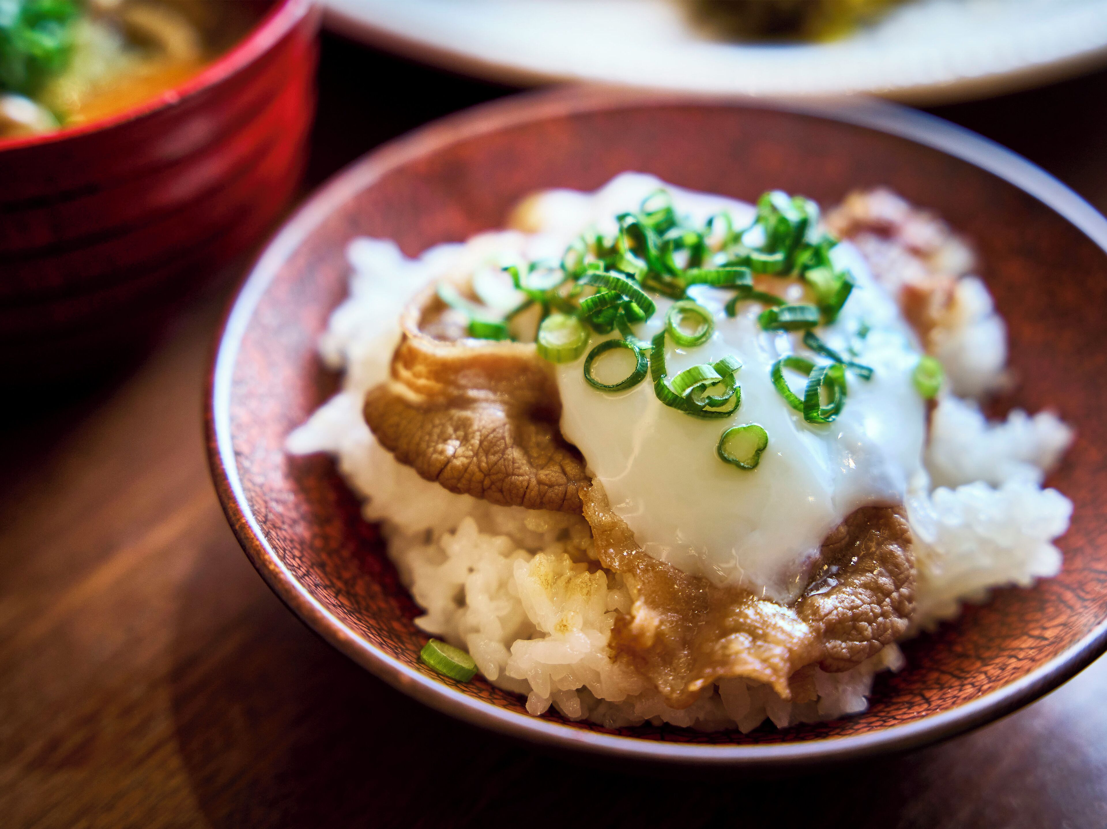 A bowl of rice topped with a slice of meat and a dollop of sauce, garnished with green onions.