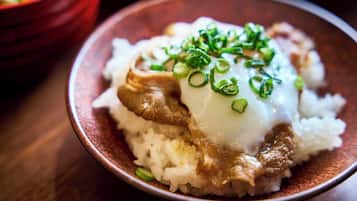 A bowl of rice topped with a slice of meat and a dollop of sauce, garnished with green onions.