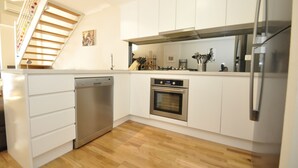 A modern kitchen with white cabinets, stainless steel appliances, and a wooden staircase. - Darlinghurst Popular Apartments (Surry Hills)