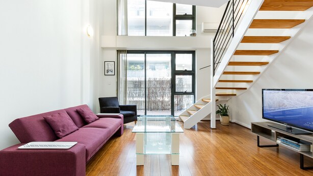 A modern living room with a wooden staircase, a glass coffee table, a sofa, and a television. - Darlinghurst Popular Apartments (Surry Hills)