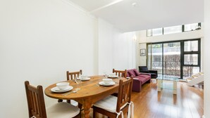 A dining area with a wooden table set for four, surrounded by chairs with cushioned seats. - Darlinghurst Popular Apartments (Surry Hills)