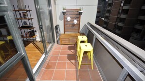 A small balcony with a wooden stool, a small table, and a shelf with books and a clock. - Darlinghurst Popular Apartments (Surry Hills)