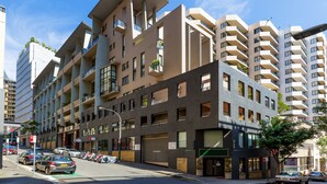 A multi-story building with balconies, a garage, and a street view with parked cars and a clear sky. - Darlinghurst Popular Apartments (Surry Hills)