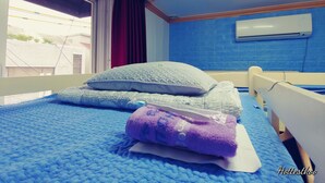 Una habitación con cama, ventana con cortinas, pared azul y aire acondicionado.