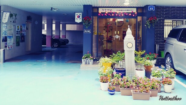 Entrada de un hotel con una torre de reloj, plantas en macetas y un letrero que dice 'Bienvenido'.