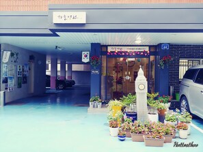 L’entrée d’un hôtel, avec un beffroi servant de cadran, des plantes en pot et une pancarte « Bienvenue ».