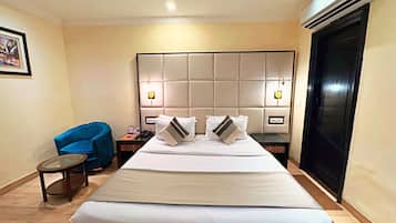 A hotel room with a large bed, a headboard with built-in lighting, a small round table, a blue chair, and a black wardrobe.