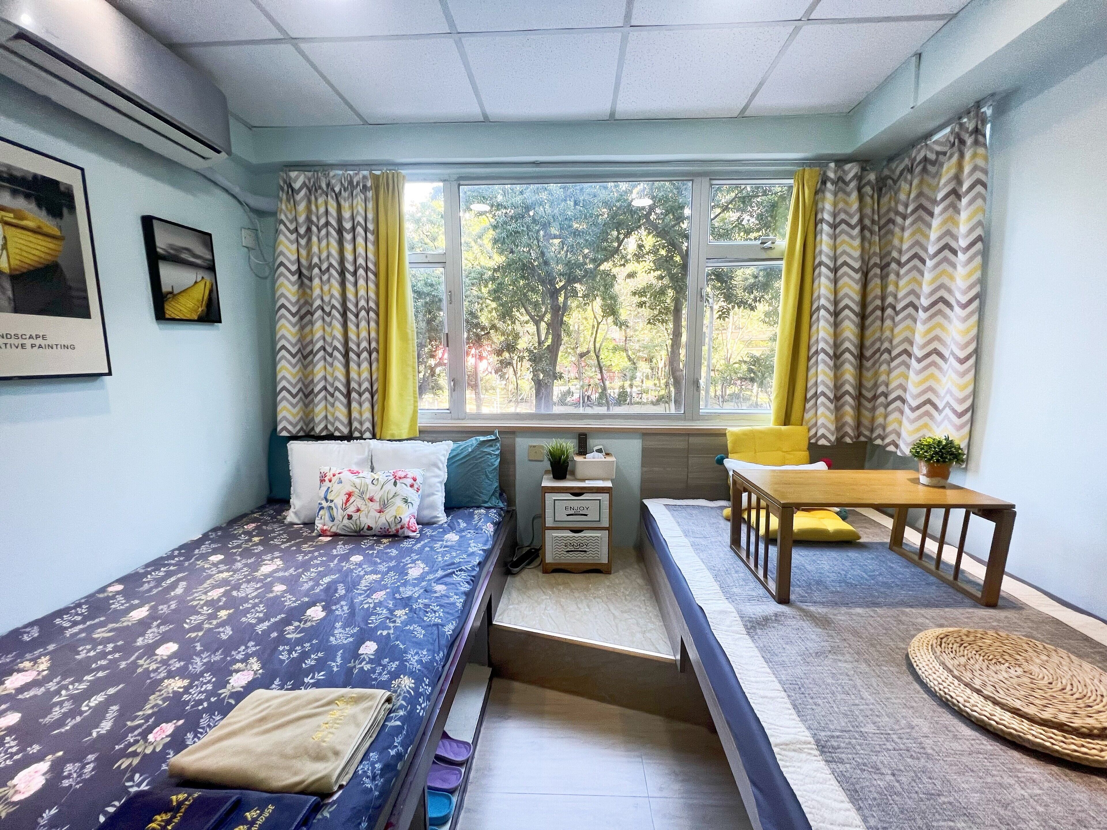 A compact room with a bed, a small table, a bench, and a window with curtains.