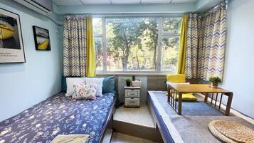 A compact room with a bed, a small table, a bench, and a window with curtains.