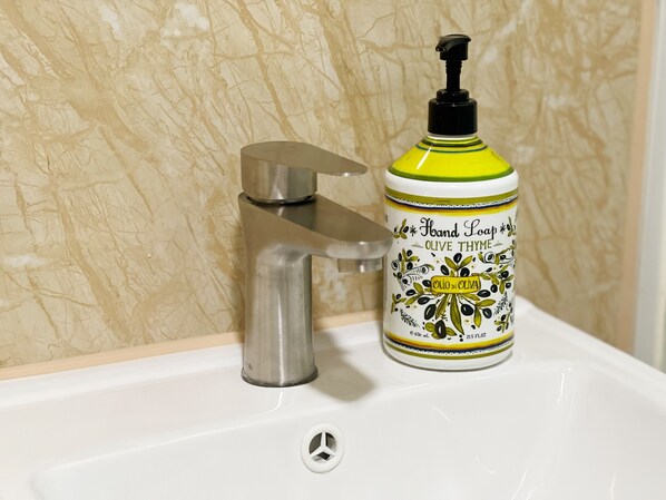 A bathroom sink with a hand soap dispenser labeled "Hand Soap Olive Thyme" and a modern faucet. - AMU Dreamhouse - Hostel (Kowloon)