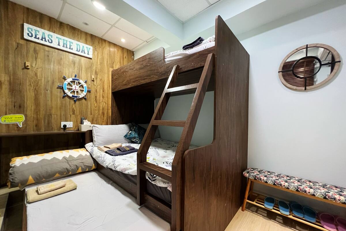 A bunk bed room with a wooden wall, a ship's wheel decoration, and a shelf with slippers.