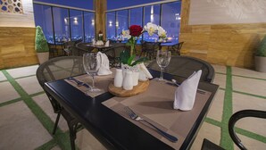 A dining table set with a rose, salt and pepper shakers, and wine glasses, with a city view in the background. - Iridium 70 Hotel (Jeddah)