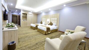 A hotel room with two beds, a sofa, a TV, and a desk with a trash can.